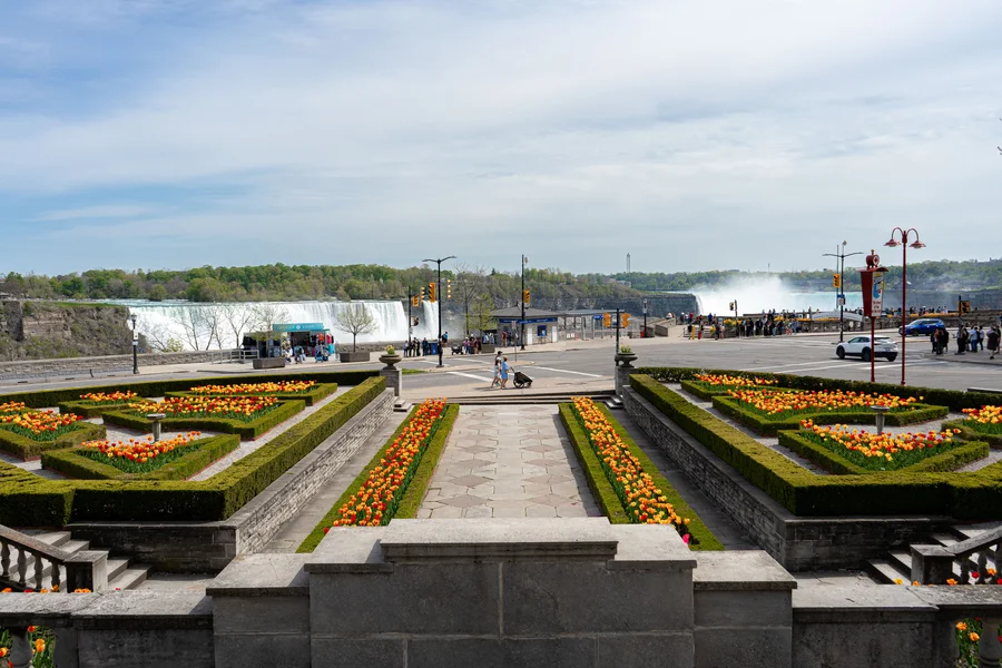 Oakes Garden Theatre spring walkway with vibrant seasonal flowers and Niagara Falls visible in the background